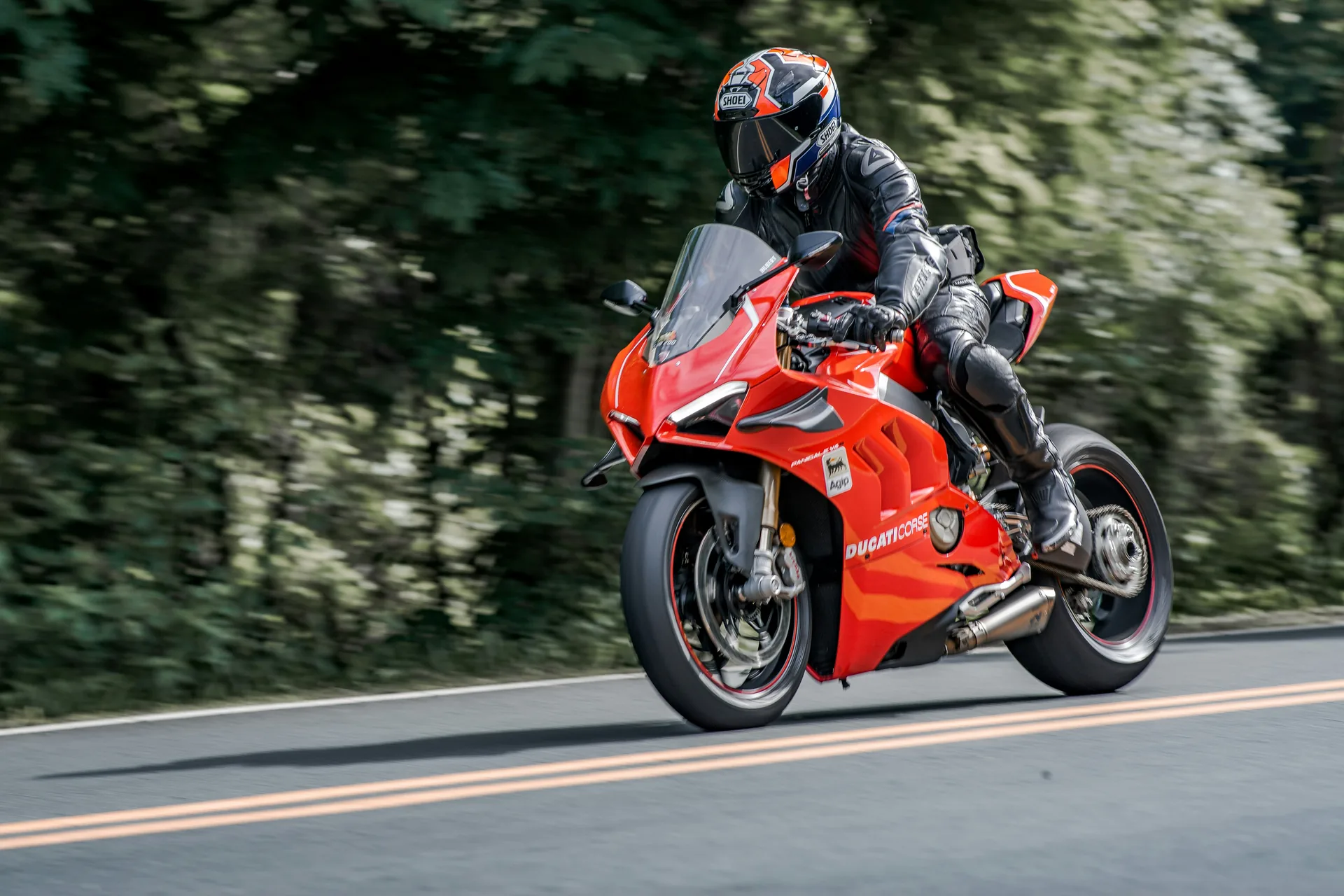 Red sport motorcycle riding on a tree-lined road