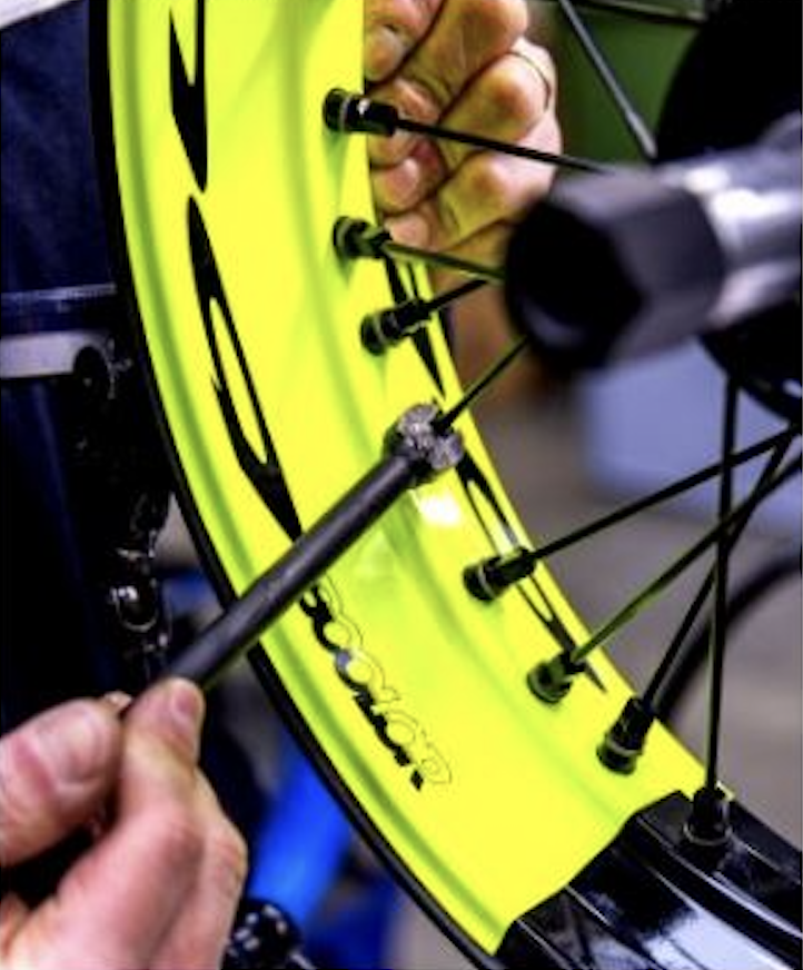 Technician manually adjusting spokes on a Pisces motorcycle wheel